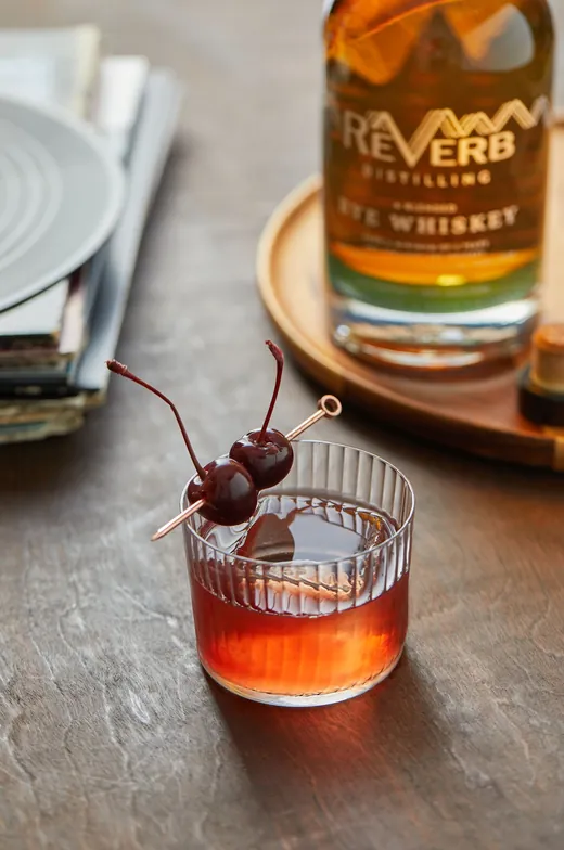 A rye Old Fashioned in a rocks glass with cherries beside ReVerb Rye