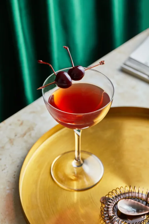 A rye Manhattan in a coupe on a gold tray beside ReVerb Rye